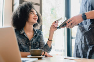 Frau hält eine Bankkarte an ein mobiles Kartenterminal im Café
