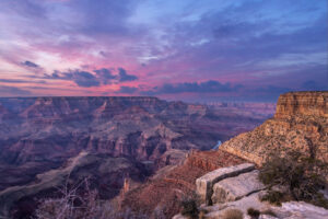 Weite Aussicht über den Grand Canyon bei Sonnenuntergang mit farbigen Wolken und tief eingeschnittenen Felsformationen.
