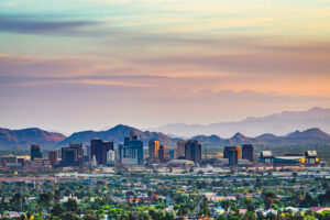 Skyline von Phoenix in Arizona in der Abenddämmerung mit Hochhäusern, Palmen und Bergkulisse unter pastellfarbenem Himmel.