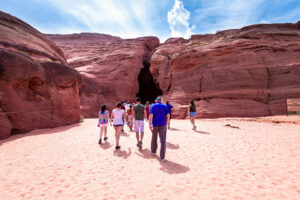 Geführte Tourgruppe läuft über sandigen Weg zum Eingang des Antelope Canyon