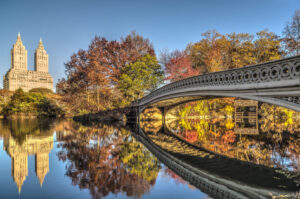 Bow Bridge im Central Park über The Lake mit Herbstlaub und Spiegelung der San-Remo-Türme
