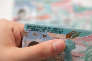 Hand hält eine US-Greencard vor einer unscharfen Permanent Resident Card im Hintergrund