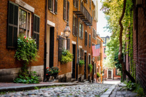 Kopfsteingepflasterte Acorn Street in Boston mit Backsteinhäusern, Fensterläden und einer US-Flagge.