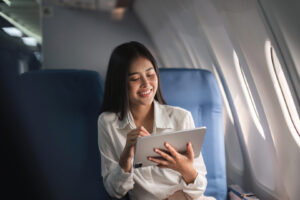 Frau nutzt ein Tablet auf einem Fensterplatz im Flugzeug.