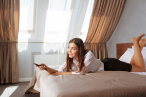 Frau liegt mit einer Fernbedienung auf einem Hotelbett.