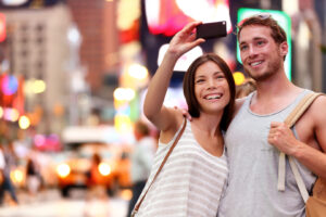 Paar nimmt mit dem Smartphone ein Selfie vor den Leuchtreklamen in New York auf.
