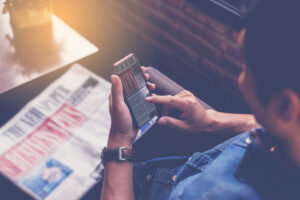Eine Person liest Nachrichten auf dem Smartphone; daneben liegt eine aufgeschlagene Zeitung.
