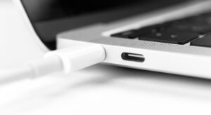 Nahaufnahme eines weißen USB-C-Ladekabels am Anschluss eines silbernen Laptops.