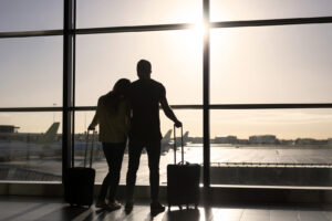 Silhouetten zweier Reisender, die im Flughafenterminal auf ihren Flug warten.